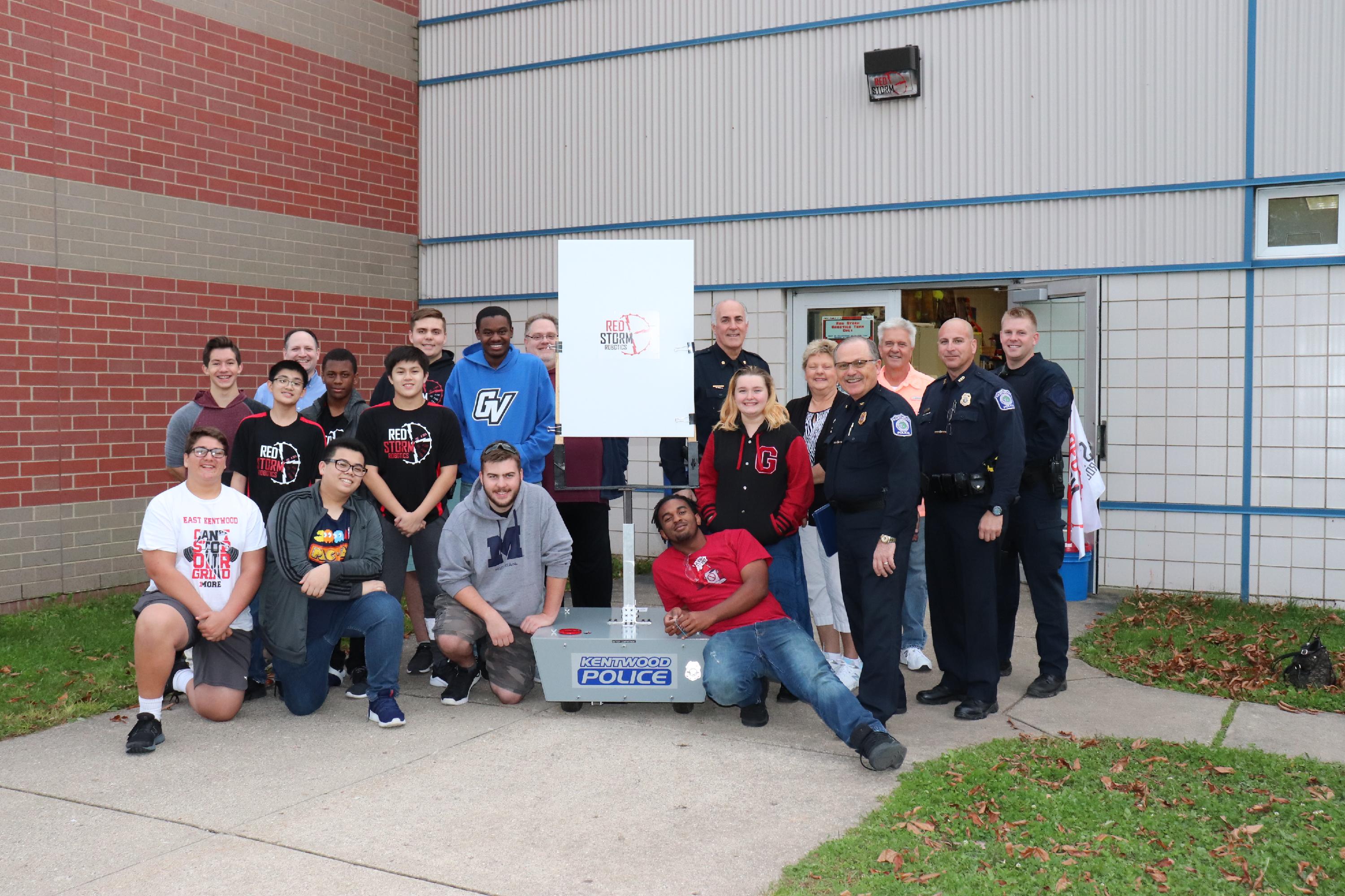 Chief Hillen, Deputy Chief Roberts, Officer Willshire, special response team member Officer Vanderbent, Kentwood Public School students, robotics team mentors and representatives from Target Solutions USA smile for a picture with the Robotic Moving Target System.